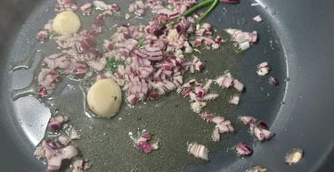 Sautéing diced red onions and garlic cloves in olive oil within a non-stick frying pan.