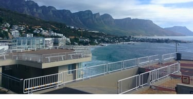 Vista costeira da Cidade do Cabo com montanhas imponentes, casas à beira-mar e o oceano ao fundo.