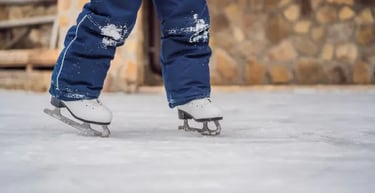 Child in blue snow pants learning to ice skate on a frozen outdoor rink.