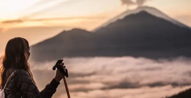 A hiker with trekking poles overlooks Mount Batur volcano at sunrise above the clouds in Bali.