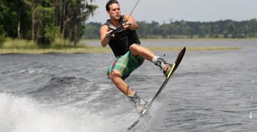 Athletic man performing a wakeboarding jump on a sunny lake with water spray.