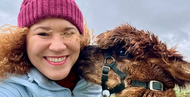Smiling woman in a purple beanie taking a selfie with a fluffy brown alpaca on a farm in Ireland.