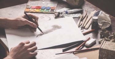 Photo of an artist working at a desk covered in art supplies