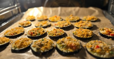 Baked eggplant rounds topped with breadcrumbs and herbs on a baking sheet inside a warm oven.