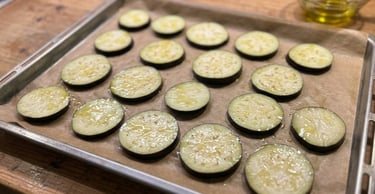 Sliced eggplant rounds brushed with olive oil on a baking sheet with parchment paper for roasting.