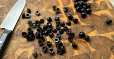 Sliced black olives on a rustic wooden cutting board with a chef's knife for food preparation.