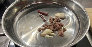Sautéing anchovies, garlic cloves, and dried chili peppers in oil in a stainless steel pan.