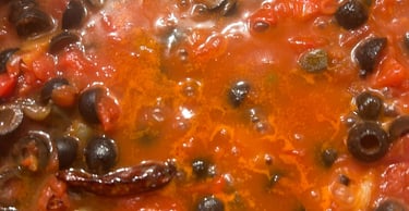 Simmering homemade puttanesca sauce with black olives, tomatoes, and garlic in a pot.