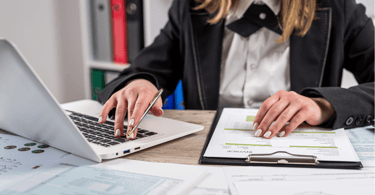 a woman in a black jacket and a laptop computer with invoices and receipt paperwork