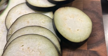 Freshly sliced raw eggplant rounds and zucchini strips on a wooden butcher block cutting board.