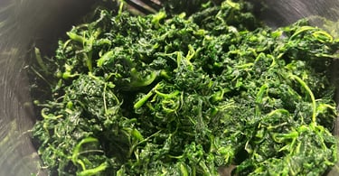 Healthy sautéed spinach leaves served in a metal bowl with a silver fork.
