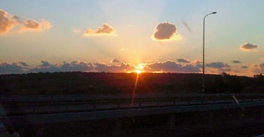 Volta de carro ao entardecer, despedida de Nazaré com o pôr do sol iluminando a estrada.