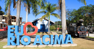 Letreiro escrito Eu Amo Rio Acima e a estação ferroviaria com um trem ao lado