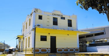 Fachada de dois andares pintada de amarelo com base marrom da antiga estação de trem em Carandaí