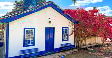 Árvore florida, casa branca e azul com dois bancos na frente, ponto turistico na Vila do Biribiri