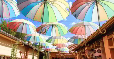 Guarda-chuvas coloridos suspensos sobre rua de lojas em Bichinho, MG, criando um corredor