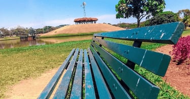 Banco de cor verde, água, ilha com moinho de vinho no alto e céu azul, no Parque Ipanema em Ipatinga