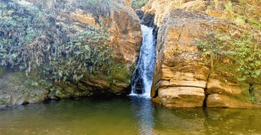 Queda d'água e grandes rochedos caindo em um poço verde na Cachoeira de Carrancas, Acuruí Itabirito