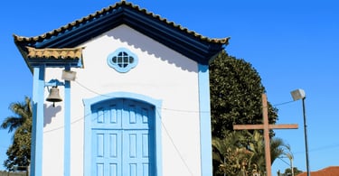 Capela branca com detalhes azuis, sino lateral e cruzeiro de madeira em Ouro Branco, Minas Gerais