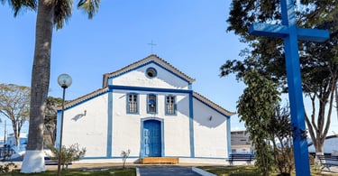 Capela branca com detalhes azuis e cruzeiro em praça de Ibituruna, em Minas Gerais