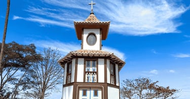 Capela em Milho Verde MG com torre colonial, cruz no alto, árvores secas e céu azul com nuvens