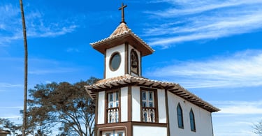Capela em Milho Verde com fachada branca, detalhes em marrom e céu azul ao fundo