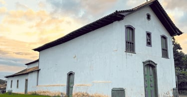 Capela do Rosário em Catas Altas MG com fachada colonial branca, portas verdes e céu ao entardecer