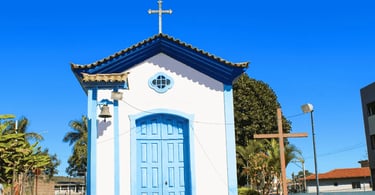 Capela em Ouro Branco MG com porta azul, cruz no jardim e céu claro ao fundo