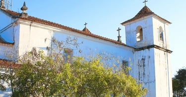 Capela histórica em Acuruí MG com fachada branca, torre lateral e vegetação ao redor em dia claro