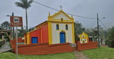 Igreja do Rosário em Ibitipoca, com fachada branca, amarela e vermelha, portas azuis e muro ao redor
