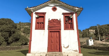 Capela em Itapanhoacanga, com fachada colonial branca e vermelha, sino e céu azul