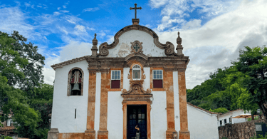 Igreja histórica localizada em Tiradentes, construção do periodo barroco com vegetação, rua de pedra