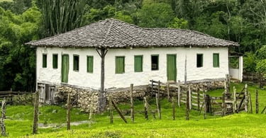 Casa rural em Gonçalves MG com paredes brancas, portas verdes, cercas de madeira e muito verde