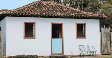 Casa simples com telhado colonial, porta azul e cadeiras na área externa em Chapada, Ouro Preto