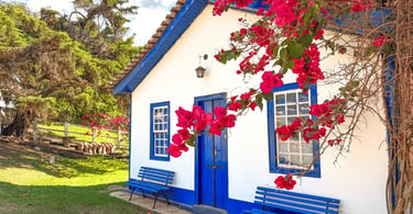 Casa colonial na Vila do Biribiri com janelas azuis, jardim gramado e flores vermelhas na fachada