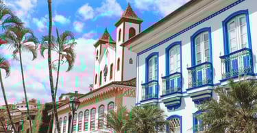 Casarões coloniais brancos com janelas azuis e uma igreja histórica ao fundo na cidade de Serro MG