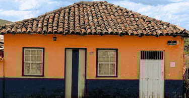 Casa colonial em Lavras Novas com fachada laranja, detalhes azuis e telhado antigo de barro