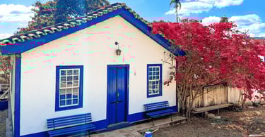 Casa de cor branca e azul, com árvore florida ao lado, na Vila do Biribiri em Diamantina MG