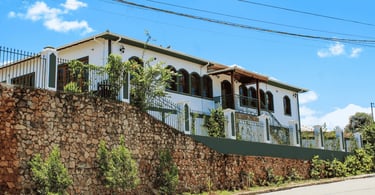 Casarão histórico branco, janelas e portas verdes, acima de um muro de pedra, Alfredo Vasconcelos