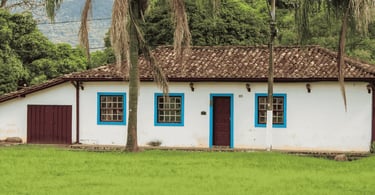 Casa colonial em Brumal MG, com janelas azuis, telhado antigo, palmeiras e gramado verde ao redor