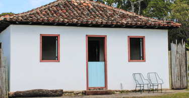 Casa histórica com duas cadeiras a frente, duas janelas e uma porta, em Chapada distrito Ouro Preto