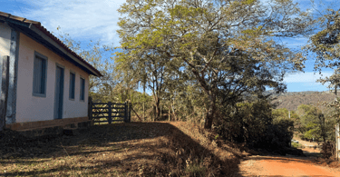 Casa histórica, porteira, árvore e uma estrada de terra em Vau, distrito histórico de Serro MG