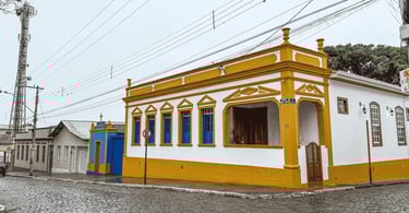 Casarão colonial amarelo e branco em esquina de rua de paralelepípedos em Entre Rios de Minas
