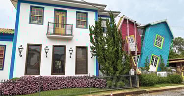 Casa colorida em Bichinho, MG, com estrutura inclinada, fachada azul e rosa e detalhes amarelos