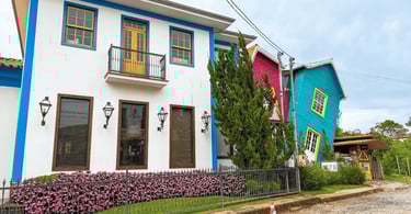 Casa Torta em Bichinho, MG, com fachada colorida inclinada ao lado de casarão branco