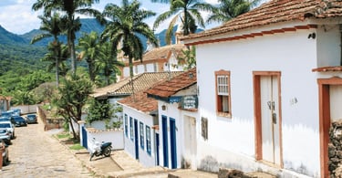 Rua de pedra em Tiradentes MG com casarões coloniais, palmeiras e montanhas ao fundo