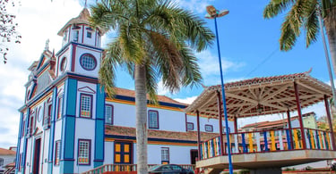 Igreja Matriz e coreto na praça central de Datas, em Minas Gerais, com palmeiras e casario ao redor