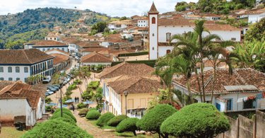 Uma escadaria descendo com pequenas árvores ao lado, casas historicas ao fundo e uma Igreja do canto