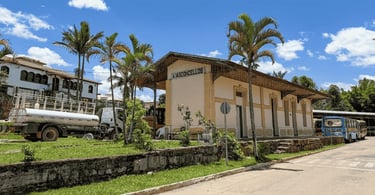 Estação Ferroviaria de Alfredo Vasconcelos, com cores amarelas e céu azul. A frente dela coqueiros