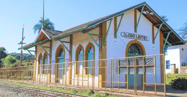 Antiga estação ferroviária, fachada branca e amarela e portas azuis ao lado de trilhos, Lobo Leite